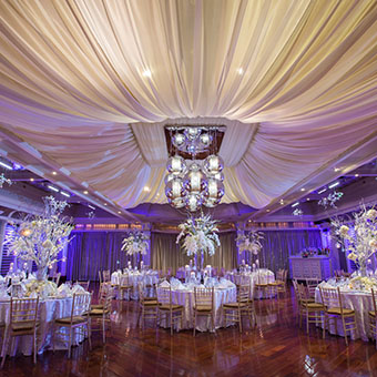 White table setup in ballroom with purple uplighting. 
